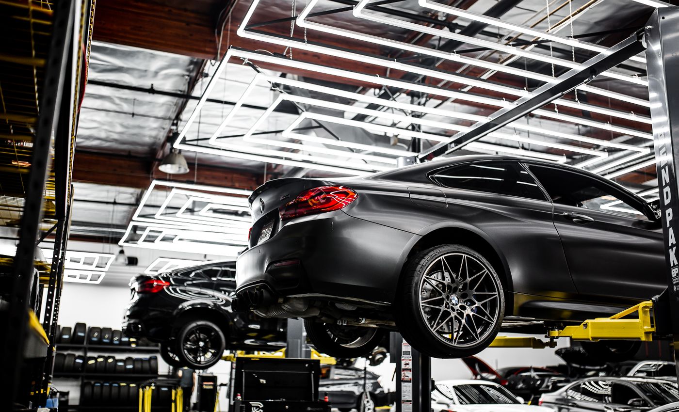 A grey BMW raised on a vehicle lift inside a brightly lit automotive workshop