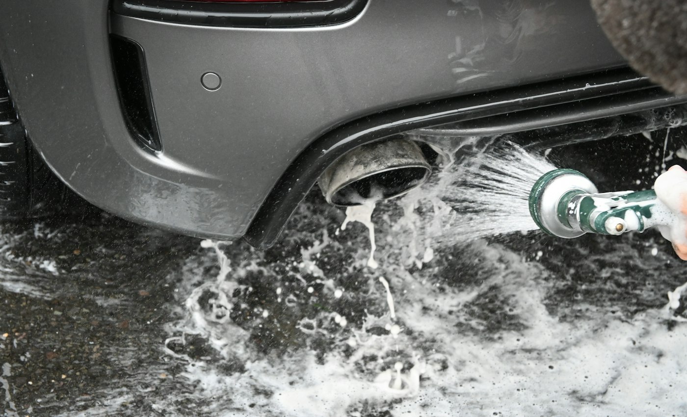 A car’s rear bumper being rinsed with a hose