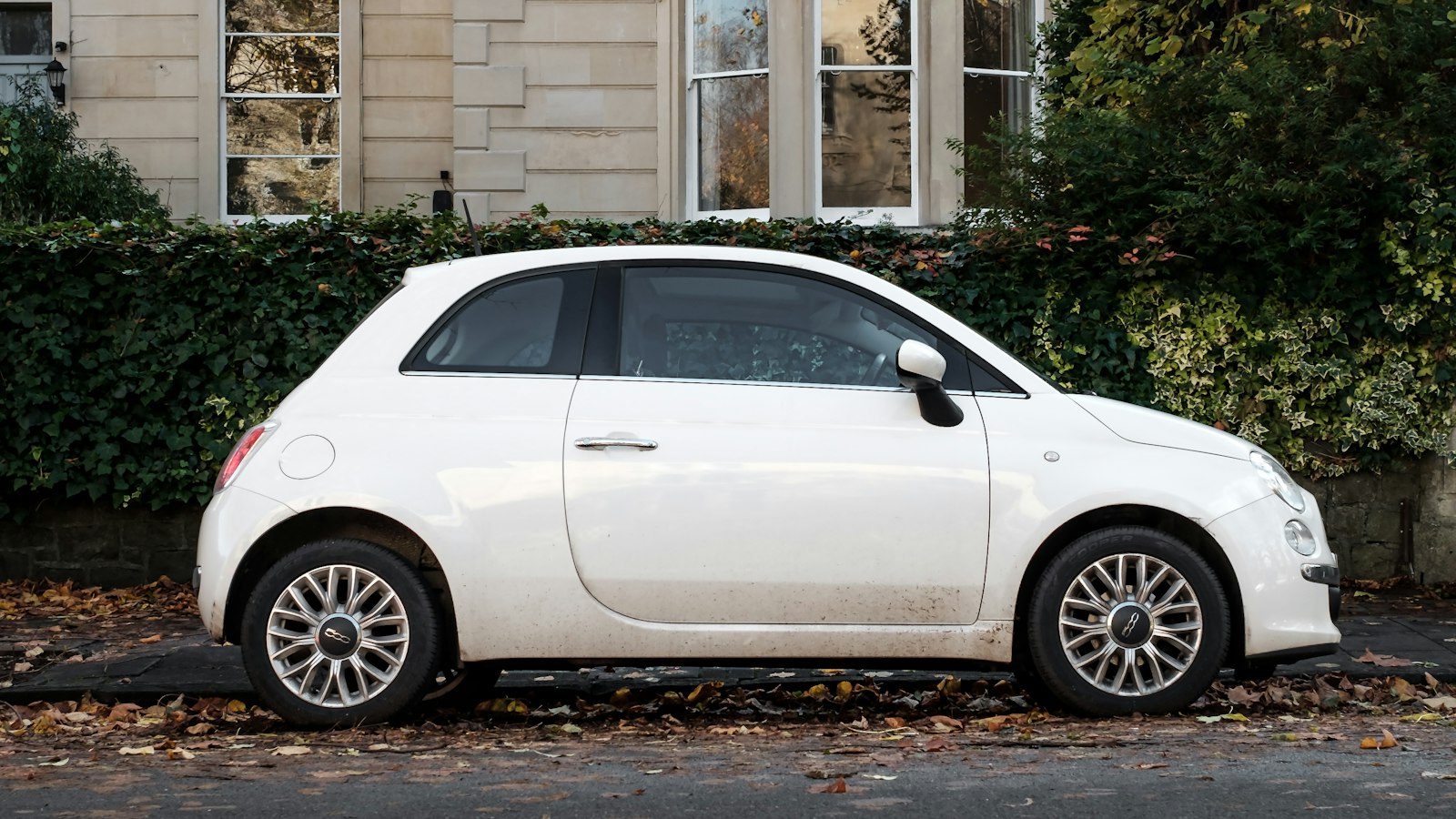 A white hatchback parked beside a building in daylight