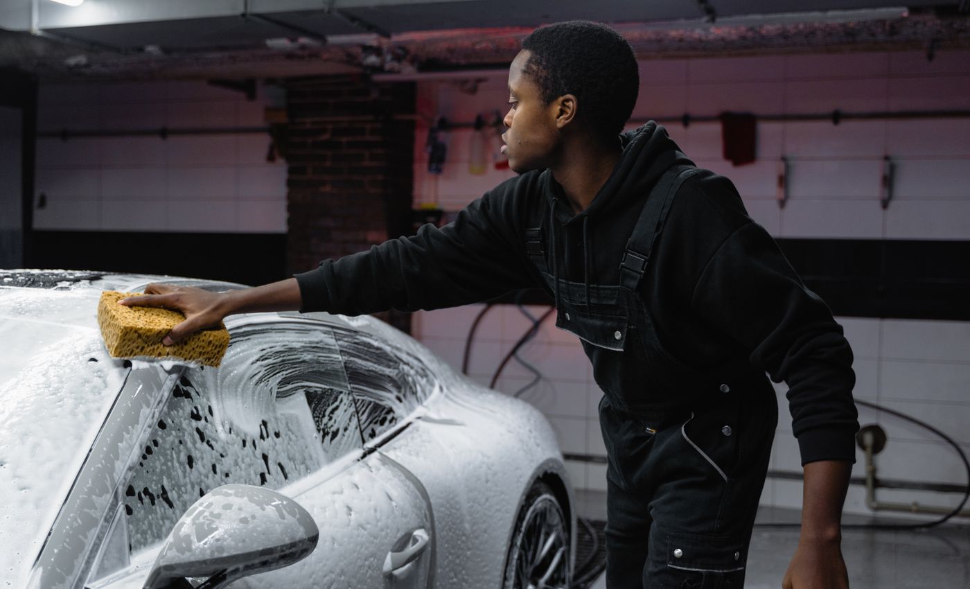 A person washing a silver car with a sponge before sale