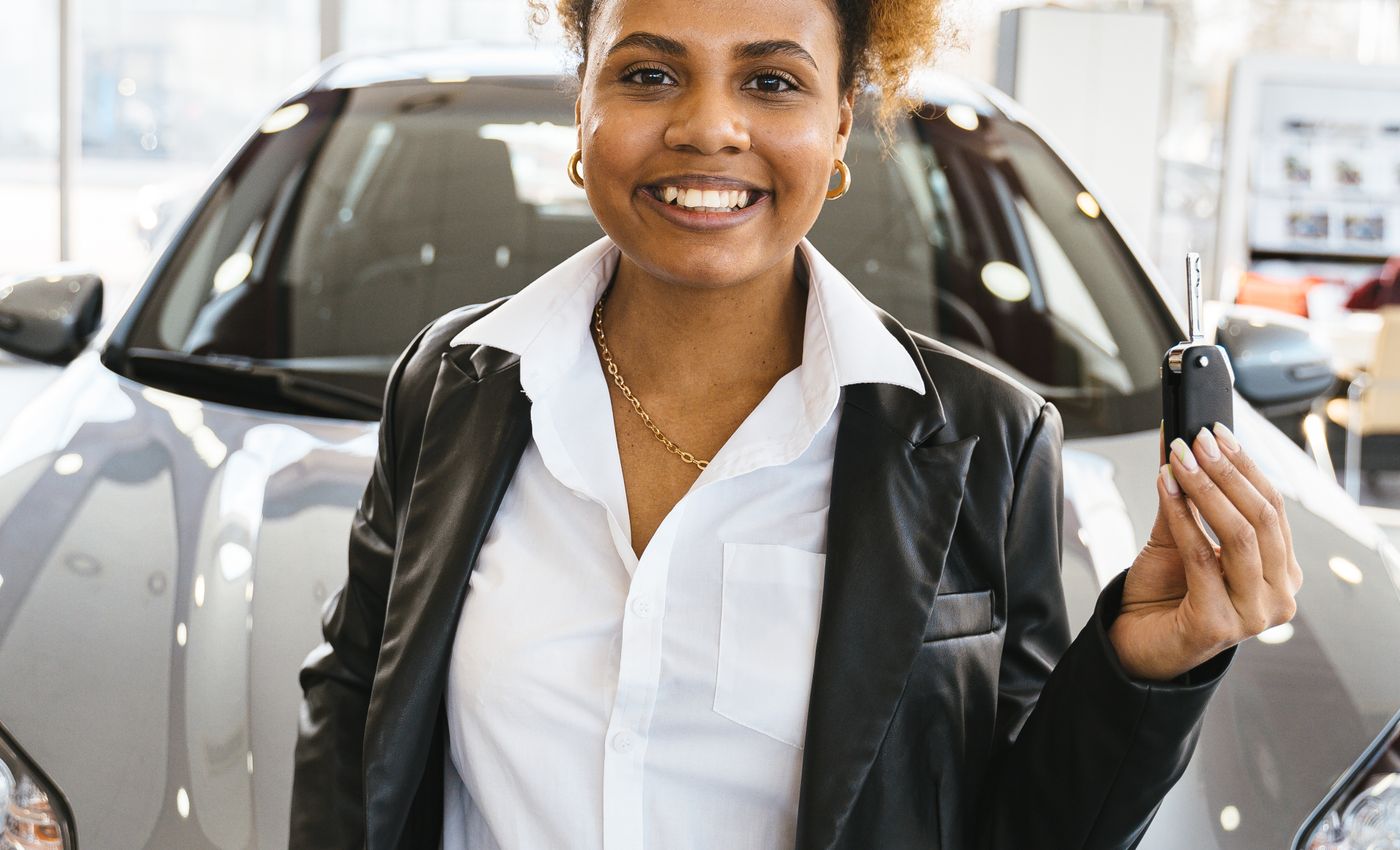 A woman holding car keys in front of a car inside a showroom